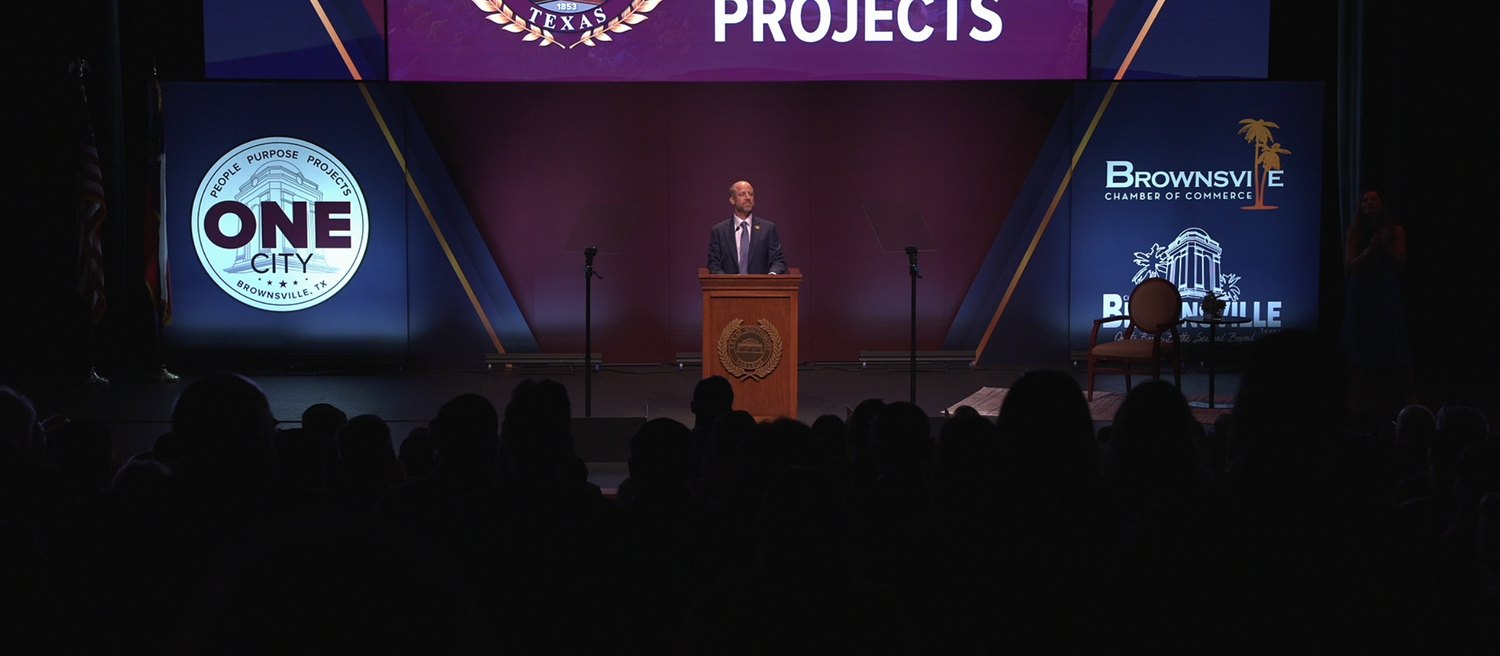 A civic address stage with three screens carrying the event's designed content above a full audience