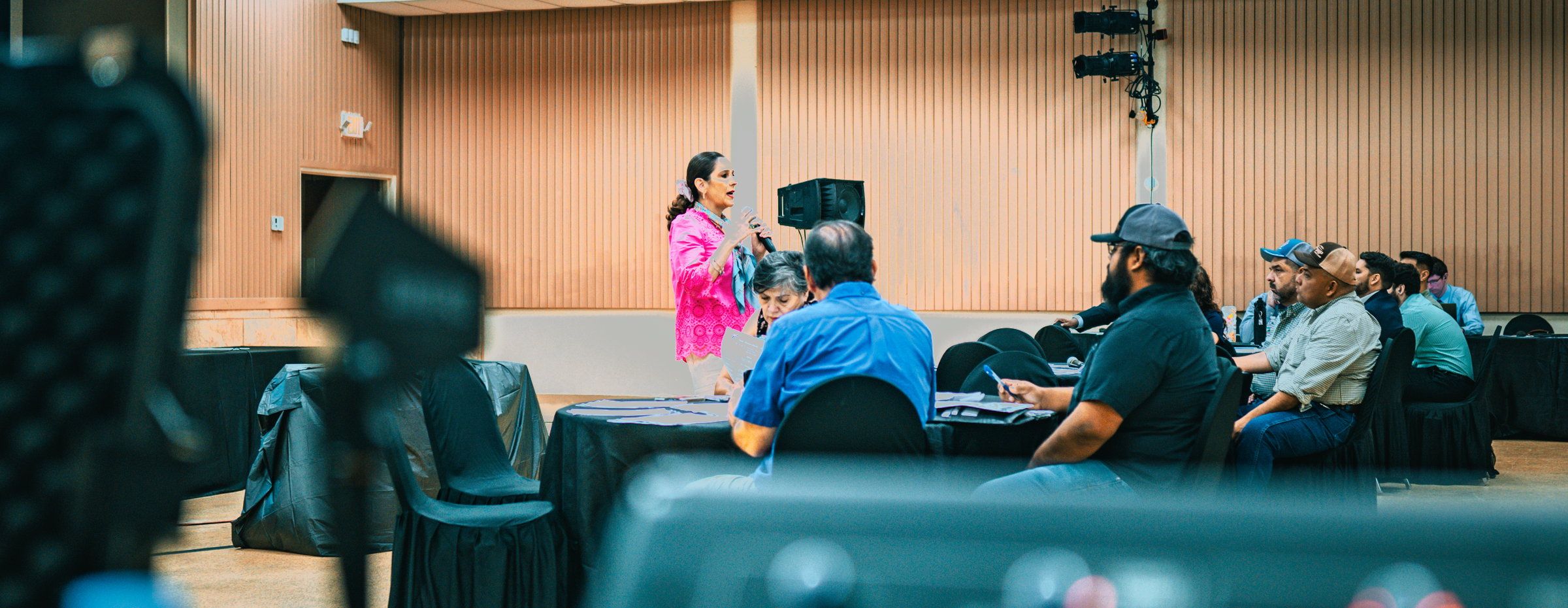 A speaker addressing a public meeting, seen past the audio console