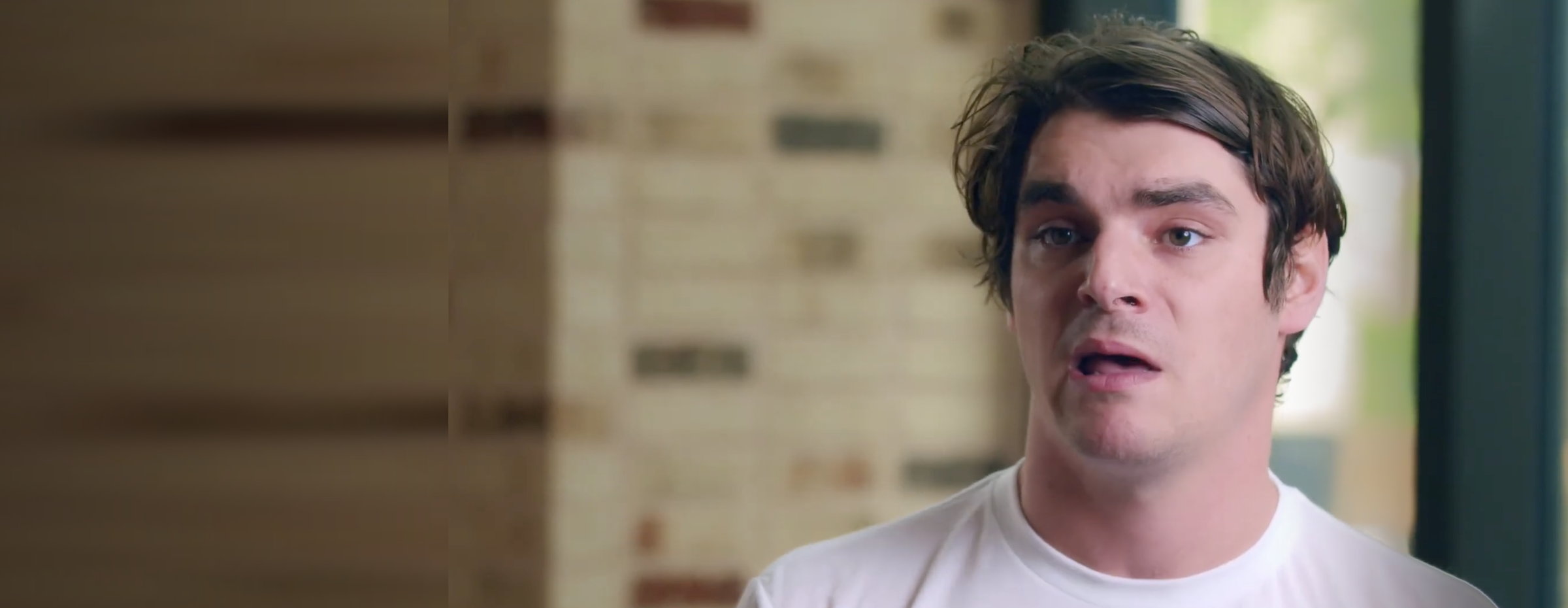 An interview subject speaking, filmed against a brick wall